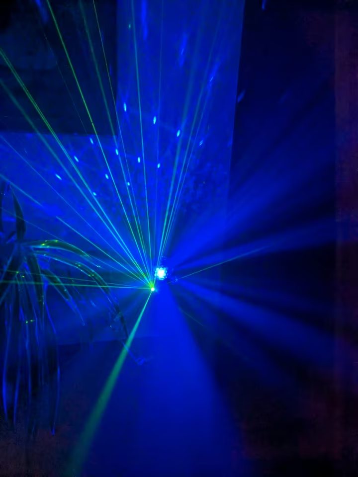 Blaue und gr&uuml;ne Lichtstrahlen der Discokugel in einem abgedunkelten Raum