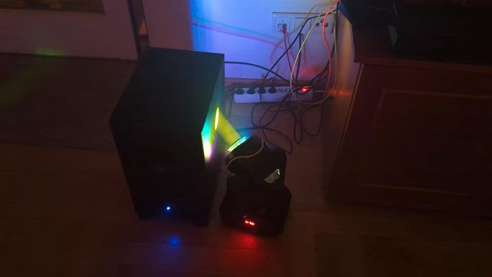 LED Moving Head mit gr&uuml;nem Lichtstrahl neben einer Box im Wohnzimmer